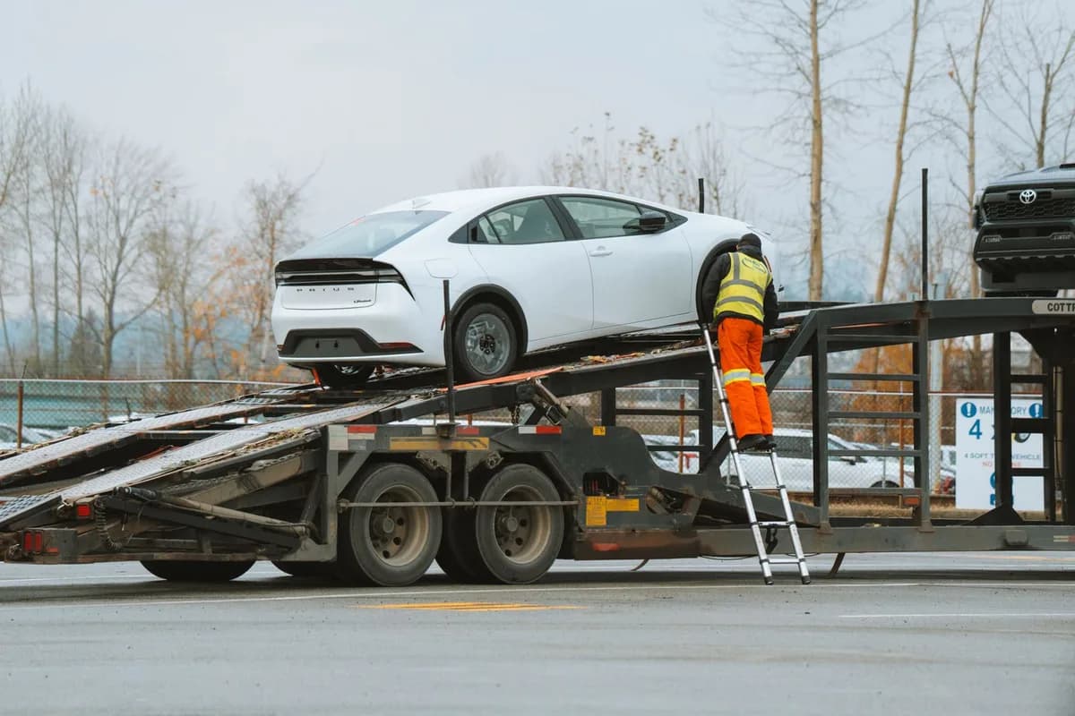 Best car shipping companies: a worker on a ladder securing a white car on the upper deck of an open car carrier trailer