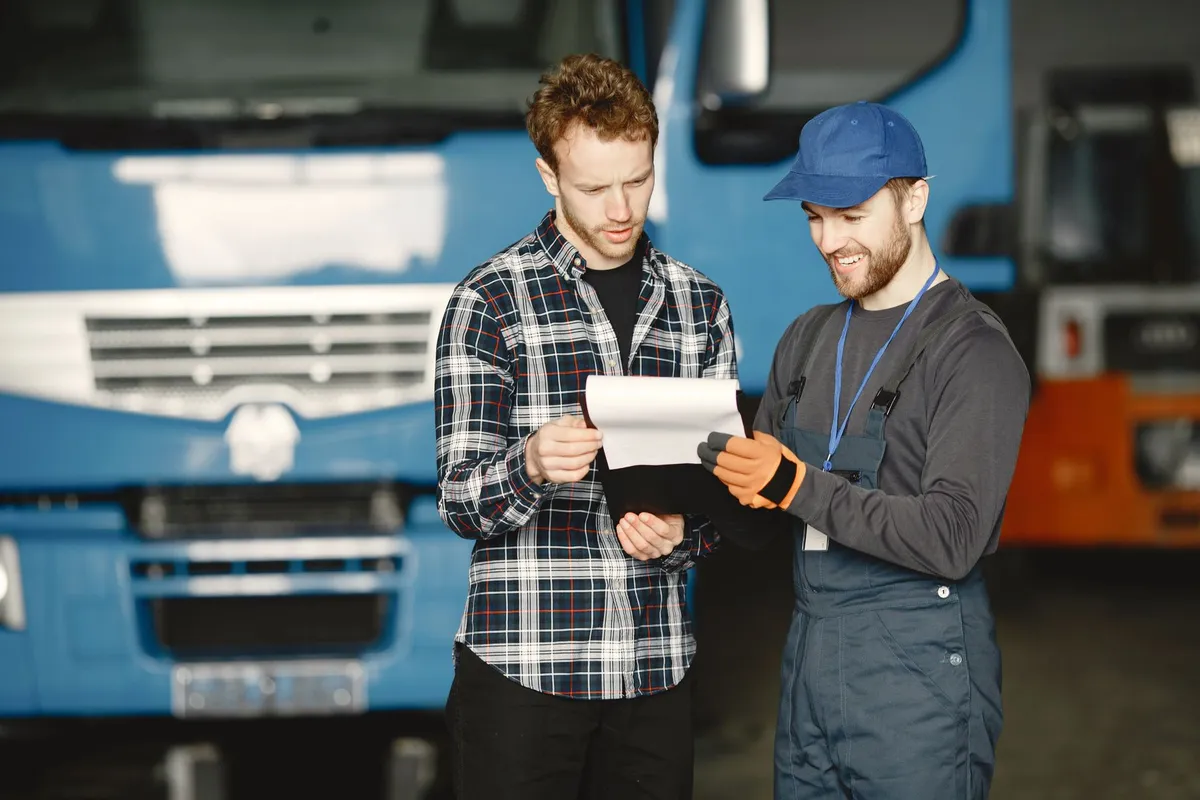 Car shipping broker vs carrier: a customer and a uniformed transport worker reviewing shipping paperwork in front of a truck