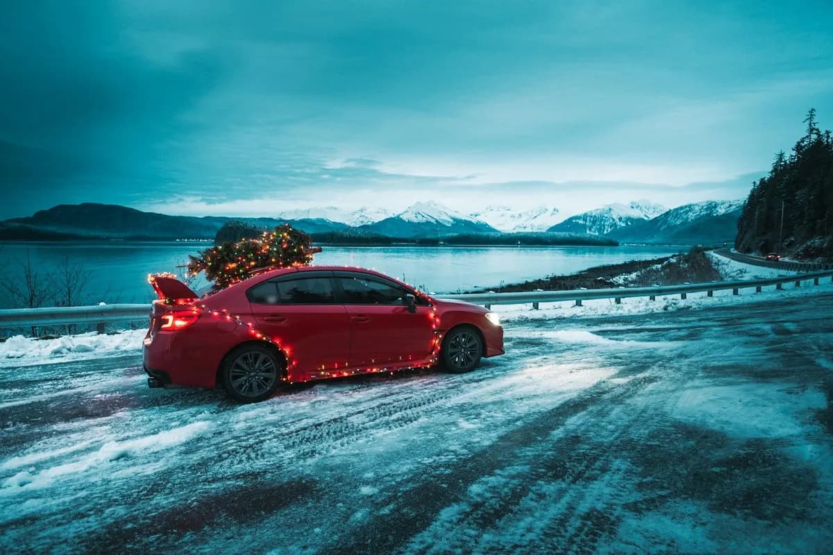 Car shipping during holidays: a red sedan with a Christmas tree on the roof parked on a snowy road at dusk