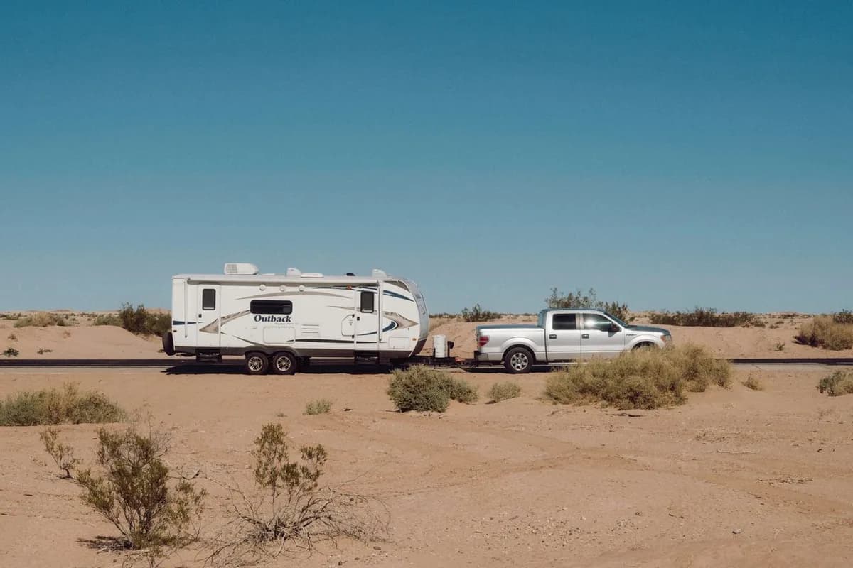 RV transport: a pickup truck towing a travel trailer on its own wheels along a desert highway